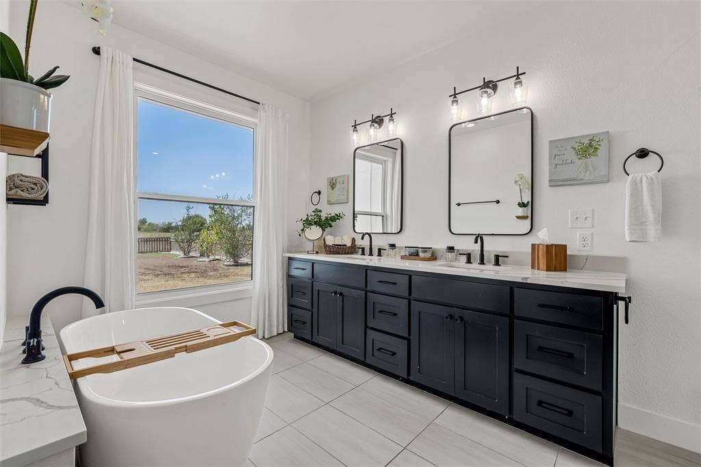 446 Wade Drive, Eddy, TX 76524 Bright bathroom featuring a freestanding tub with matte black fixtures, a dual vanity with a light-toned countertop, black cabinetry, and two rectangular mirrors