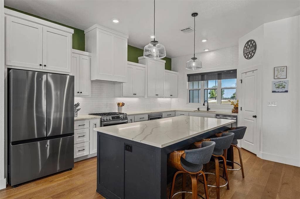 446 Wade Drive, Eddy, TX 76524 Kitchen featuring stainless steel appliances, white shaker cabinetry, an expansive island with a light-toned countertop, wood-finish flooring, and pendant lighting