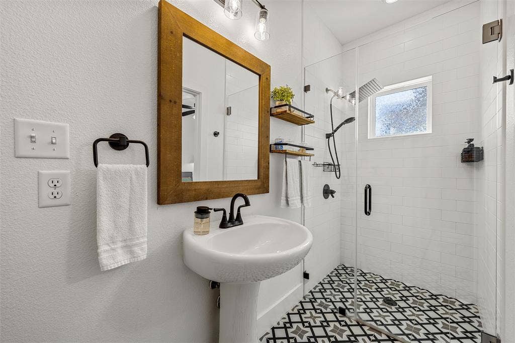 446 Wade Drive, Eddy, TX 76524 Pedestal sink with matte black faucet, framed mirror, glass-enclosed shower, shower with a rainfall head and handheld sprayer, and patterned floor tile