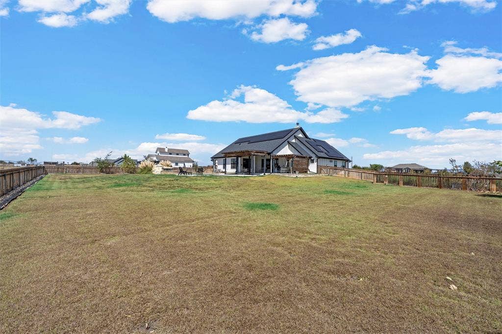 446 Wade Drive, Eddy, TX 76524 Expansive backyard featuring a partial wood fence, a single-story residence with dark roof, solar panels, and an outdoor patio with a pergola