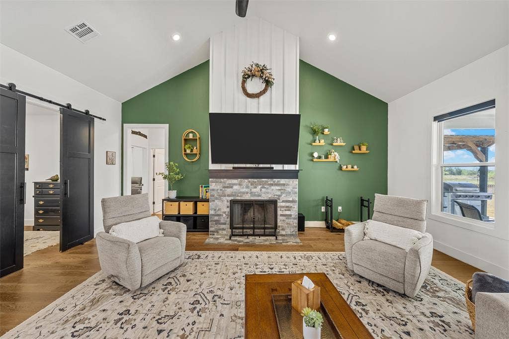 446 Wade Drive, Eddy, TX 76524 Vaulted ceiling, stone-clad fireplace, wood-finish flooring, accent wall, and sliding barn doors