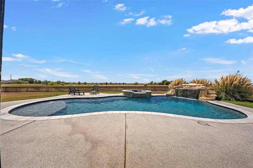 446 Wade Drive, Eddy, TX 76524 Curved swimming pool with integrated spa, concrete deck, rock waterfall feature, and surrounding landscaping