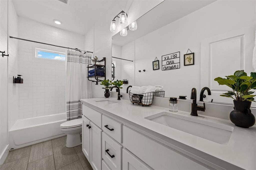446 Wade Drive, Eddy, TX 76524 Bathroom featuring a dual vanity, white cabinetry, integrated sinks, black hardware, and a tub with subway tile surround (hall bathroom)