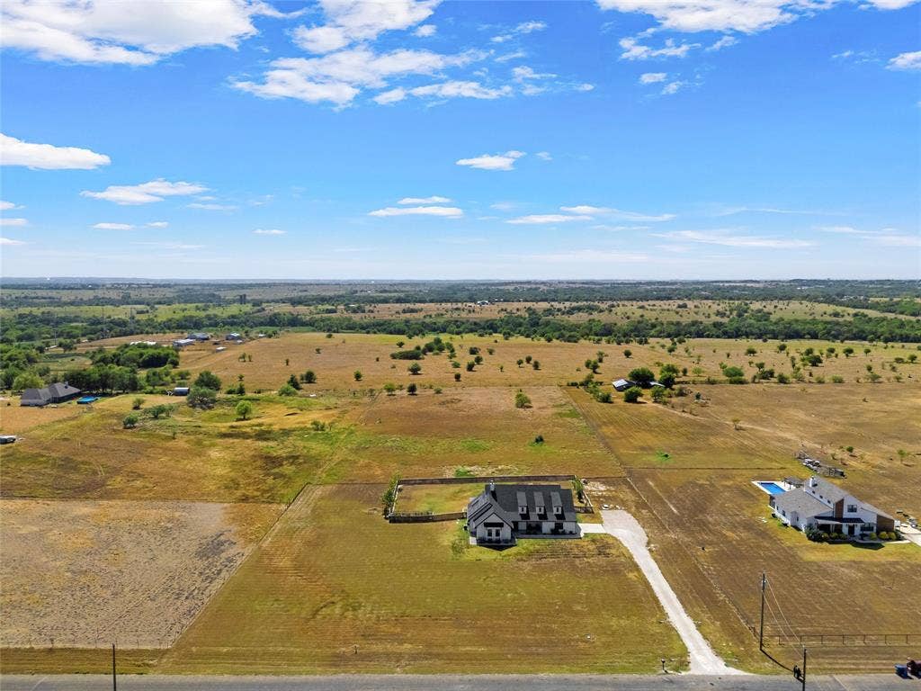 446 Wade Drive, Eddy, TX 76524 Expansive property featuring a gravel driveway, stone perimeter fencing, and a detached two-story residence with a dark gray roof