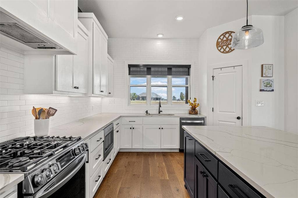 446 Wade Drive, Eddy, TX 76524 White shaker cabinetry, wood-finish flooring, stainless steel appliances, built-in microwave, and a black kitchen island