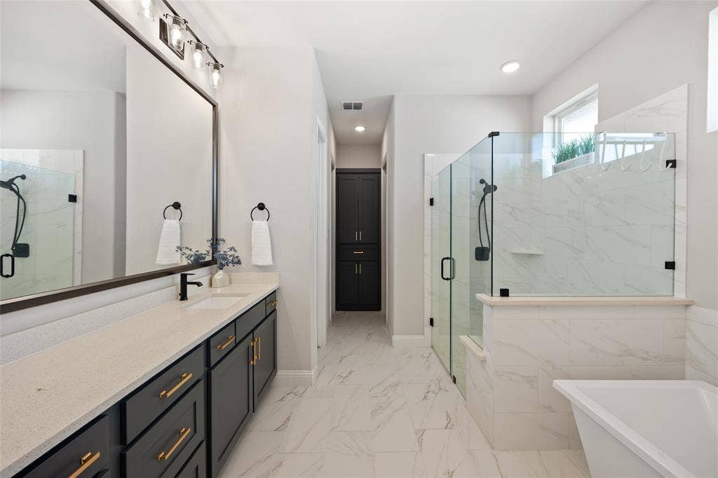 12512 Deer Trail, Frisco, TX 75035 Spacious bathroom featuring a double vanity with ample counter space, a large framed mirror, a separate glass-enclosed shower, a built-in bathtub, and floor-to-ceiling cabinetry