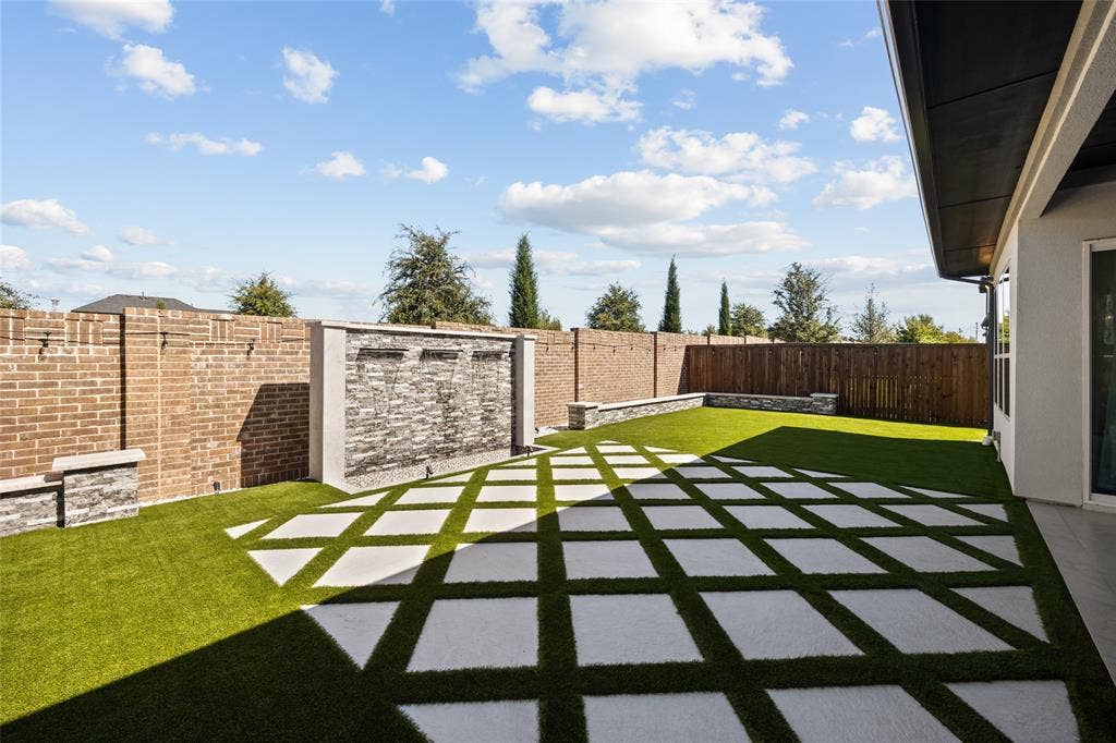 12512 Deer Trail, Frisco, TX 75035 Expansive backyard featuring a brick perimeter wall, stacked stone water feature, artificial turf, and geometric paver patio