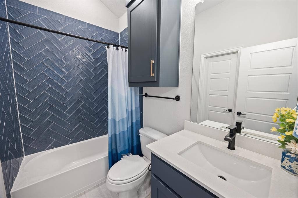 12512 Deer Trail, Frisco, TX 75035 Bathroom featuring a built-in tub with a blue herringbone tile surround, dark blue cabinetry, a white countertop, and a built-in mirror