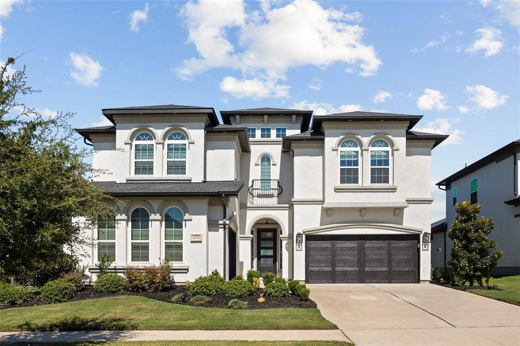 12512 Deer Trail, Frisco, TX 75035 Stucco exterior with arched windows, dark-frame garage doors, and a decorative balcony