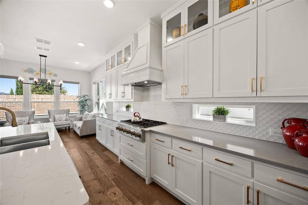 12512 Deer Trail, Frisco, TX 75035 White shaker cabinetry with gold-tone hardware, wood-finish flooring, white diamond-patterned backsplash, and integrated stainless steel appliances