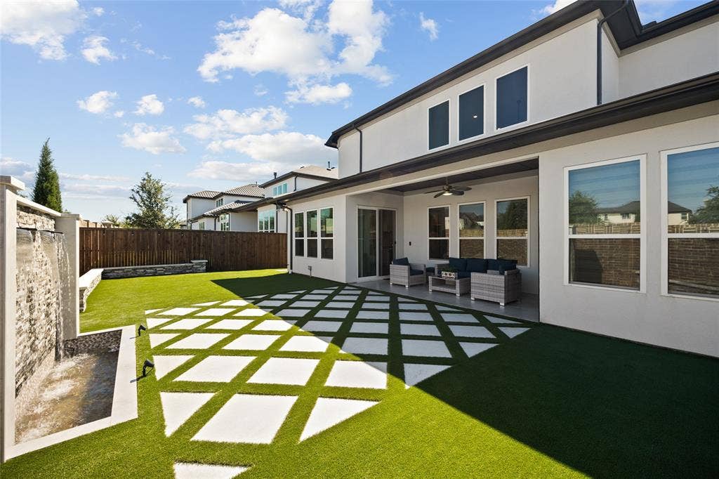 12512 Deer Trail, Frisco, TX 75035 Private backyard featuring a stone-clad water feature, artificial turf, modern patio pavers, and a covered patio with an outdoor ceiling fan