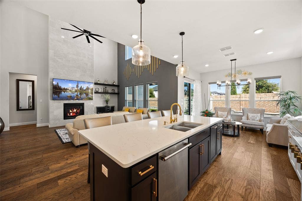 12512 Deer Trail, Frisco, TX 75035 Expansive open-concept living area featuring high ceilings, wood-finish flooring, a contemporary fireplace with a full-height surround, and an island kitchen with a dishwasher and under-mount sink
