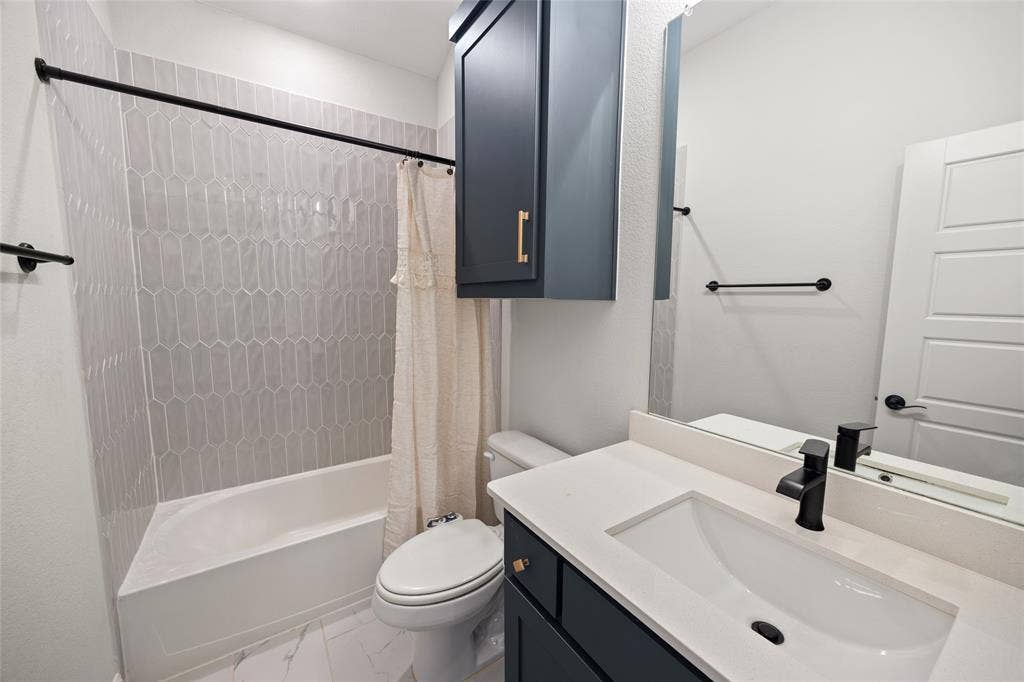 12512 Deer Trail, Frisco, TX 75035 White bathroom featuring a single vanity with a white countertop and dark cabinet, a built-in tub with light grey elongated hexagonal tile surround, and a wall-mounted mirror