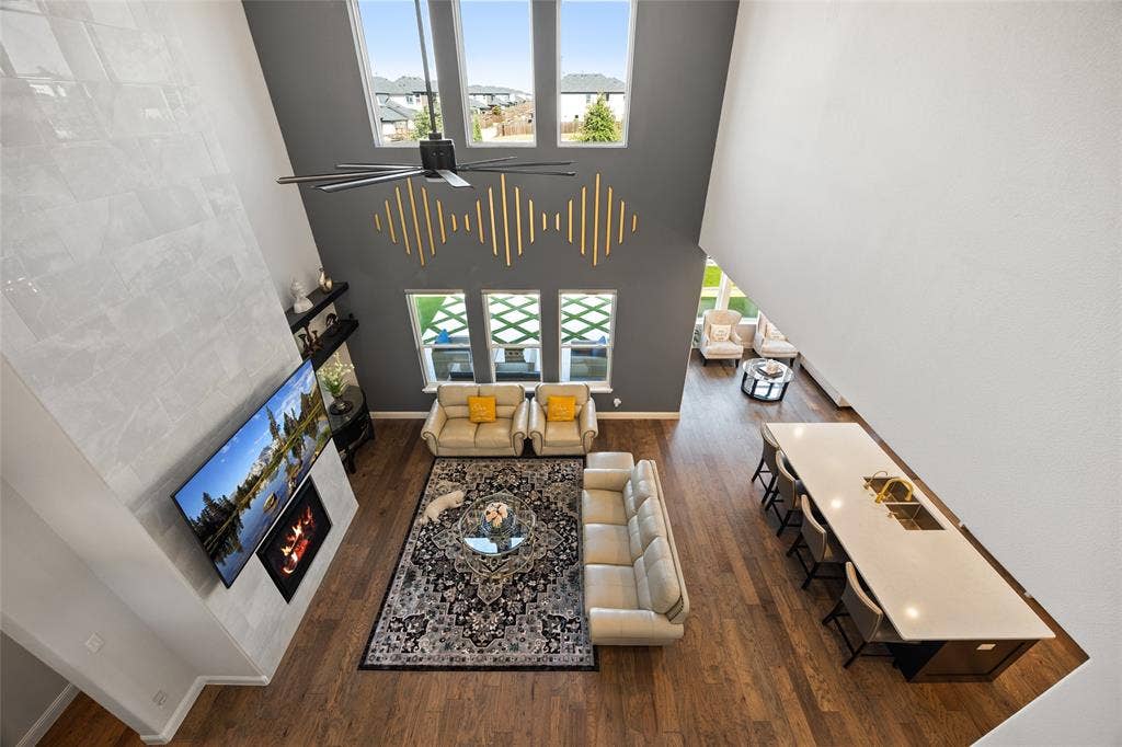 12512 Deer Trail, Frisco, TX 75035 Double-height great room featuring a tall tiled fireplace surround, high ceilings, wood-finish flooring, and an expansive kitchen island with seating