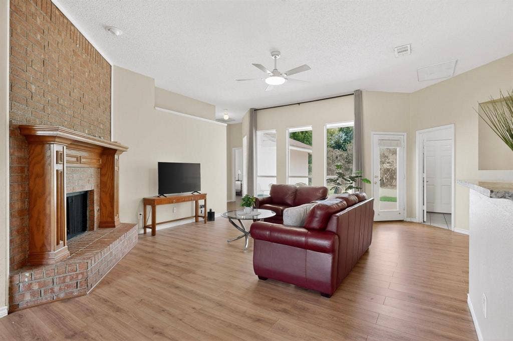 320 Elizabeth Trail, Murphy, TX 75094 Living area featuring wood-finish flooring, a brick-surround fireplace with a wood mantle, a ceiling fan, and multiple large windows