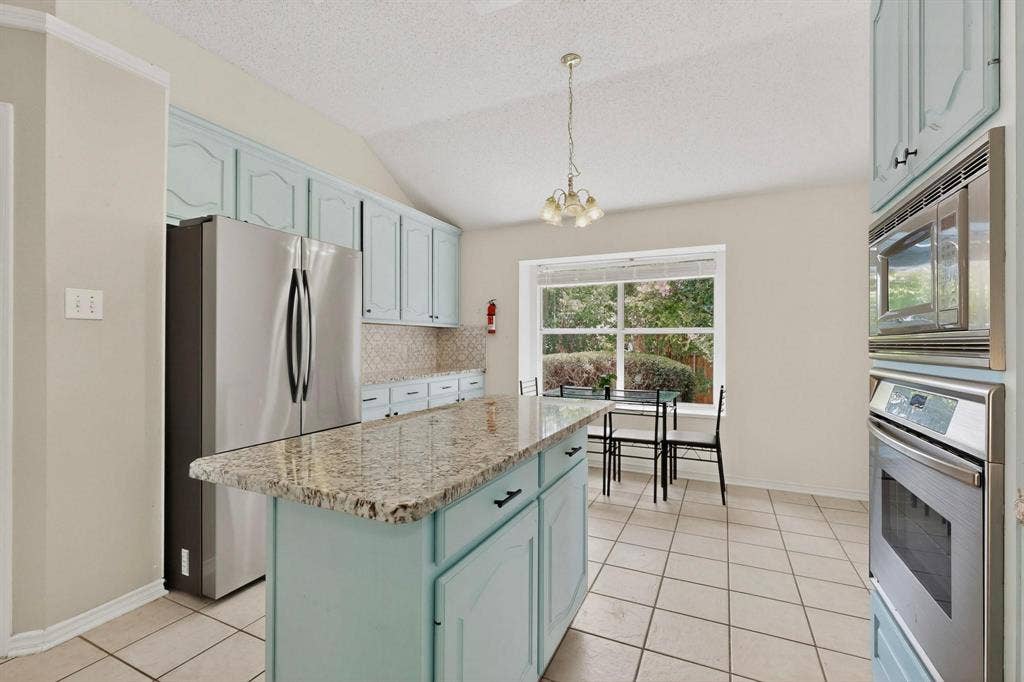 320 Elizabeth Trail, Murphy, TX 75094 Kitchen featuring a central island with a speckled countertop, light blue cabinetry, tiled flooring, and a large window