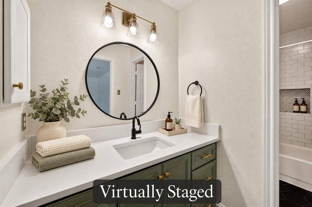 4448 Cleveland Drive, Plano, TX 75093 The updated primary bath features a green vanity, a crisp white countertop, a round mirror and stylish mixed-metal accents. Virtually staged.