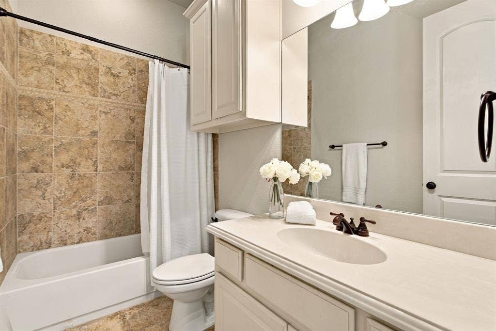 Bathroom featuring a tub-shower combination with ceramic tile surround, integrated vanity with a solid-surface countertop, oval undermount sink, and wall-mounted cabinetry