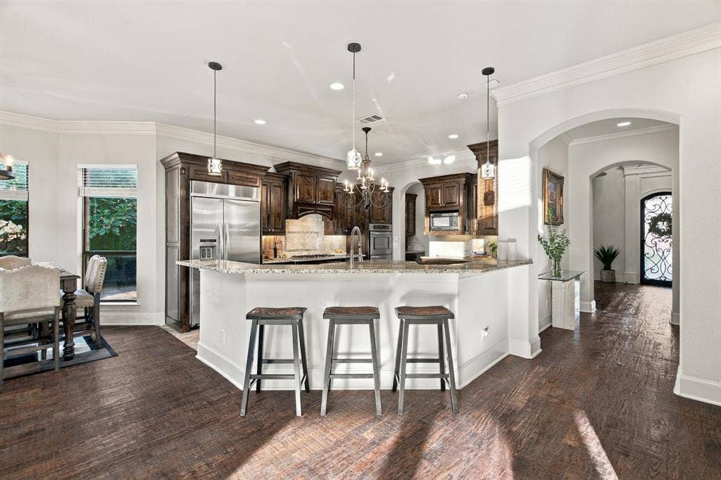 Kitchen featuring dark wood cabinetry, stainless steel appliances, stone countertops, wood-finish flooring, and crown molding