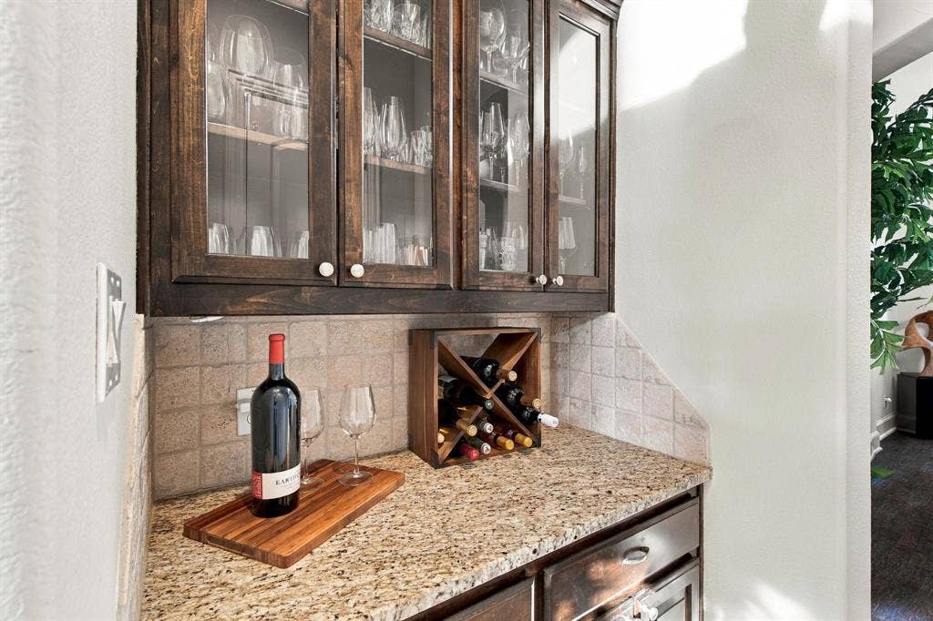 Built-in bar featuring stained wood cabinetry with glass-front uppers, stone countertops, and a tiled backsplash