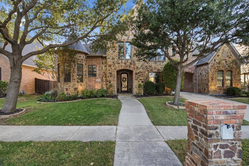 Exterior facade featuring natural stone masonry, a turret-style architectural element, arched entryway, and concrete walkway