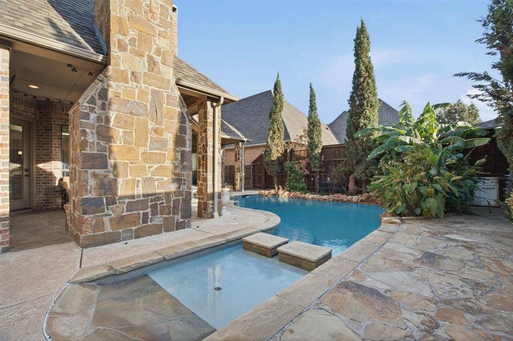 Outdoor living area featuring a covered patio, a masonry fireplace, a swimming pool, and stone hardscaping
