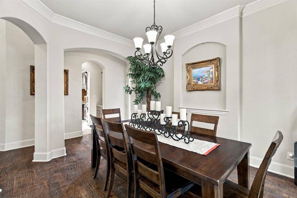 Arched architectural doorways, crown molding, wood-finish flooring, iron chandelier, and a recessed wall niche