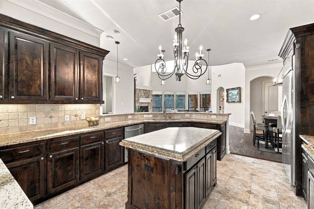 Kitchen featuring dark-finish cabinetry, natural stone countertops, a central island, tiled flooring, and a decorative wrought iron chandelier