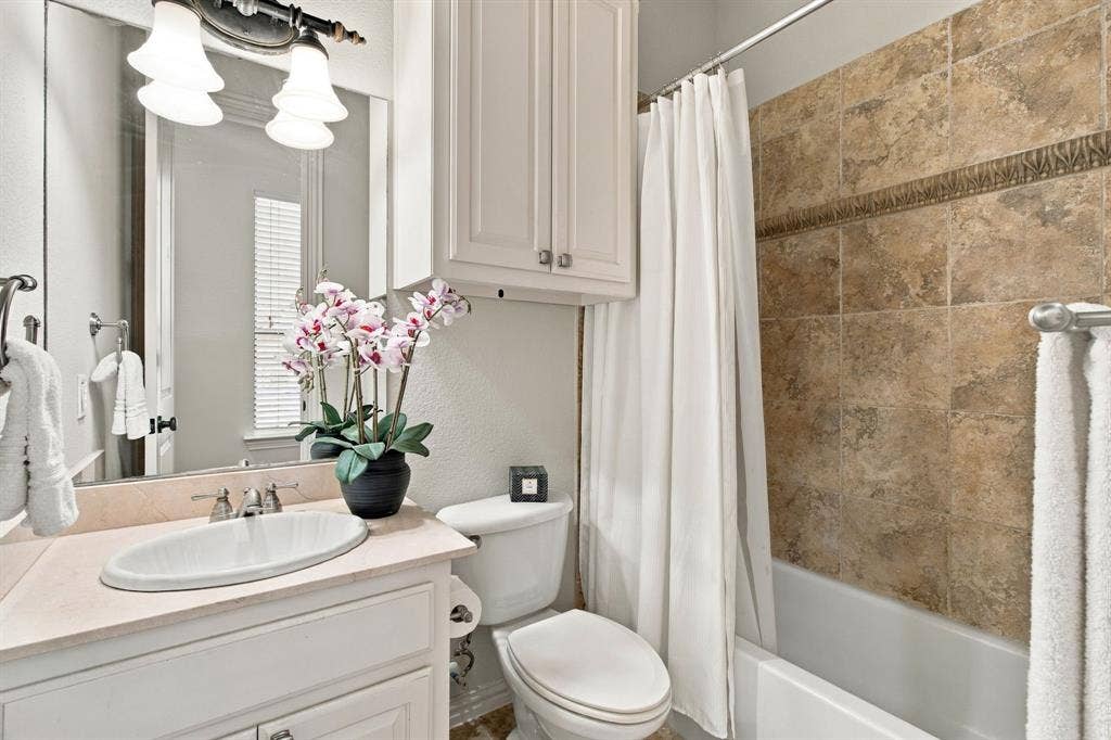 Bathroom featuring an oval undermount sink with integrated countertop, white Shaker-style cabinetry, a wall-mounted storage cabinet, and a tiled shower surround with decorative accent inlay