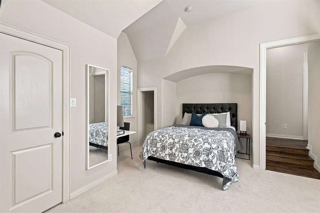 Vaulted ceiling with architectural arch niche, neutral wall-to-wall carpeting, and wood-finish flooring steps