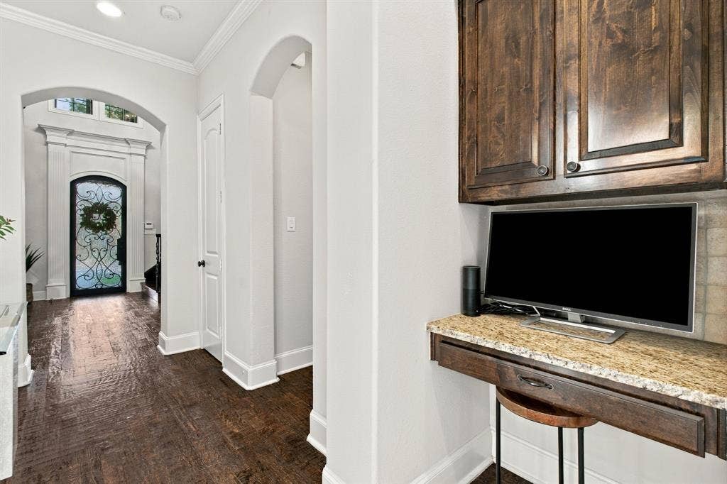Built-in workspace featuring stained wood cabinetry and stone countertop, wood-finish flooring, arched doorways, and front entry door with decorative iron inlay
