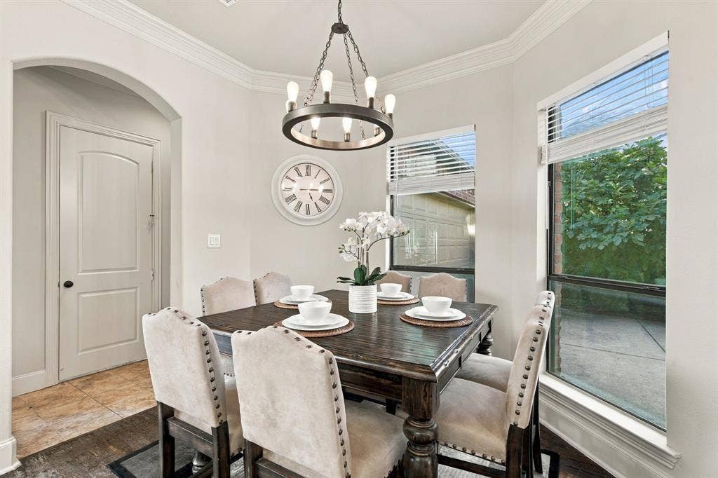 Dining area featuring crown molding, arched entryway, large windows with horizontal blinds, wood-finish flooring, and a circular metal chandelier