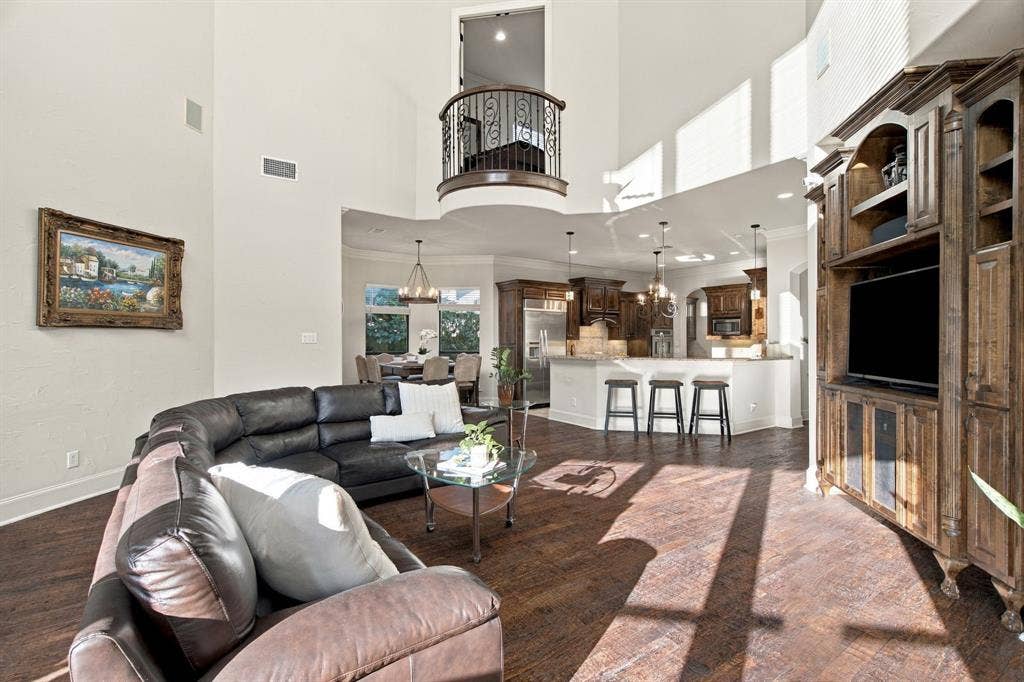 Two-story high ceiling with interior wrought-iron Juliet balcony, custom built-in dark wood cabinetry, wood-finish flooring, and recessed lighting