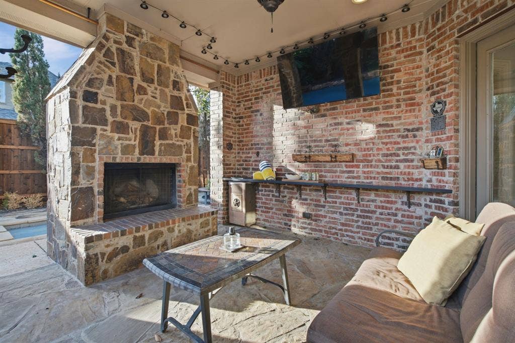 Covered outdoor living space featuring a floor-to-ceiling stone fireplace, exposed brick walls, flagstone flooring, and a built-in counter