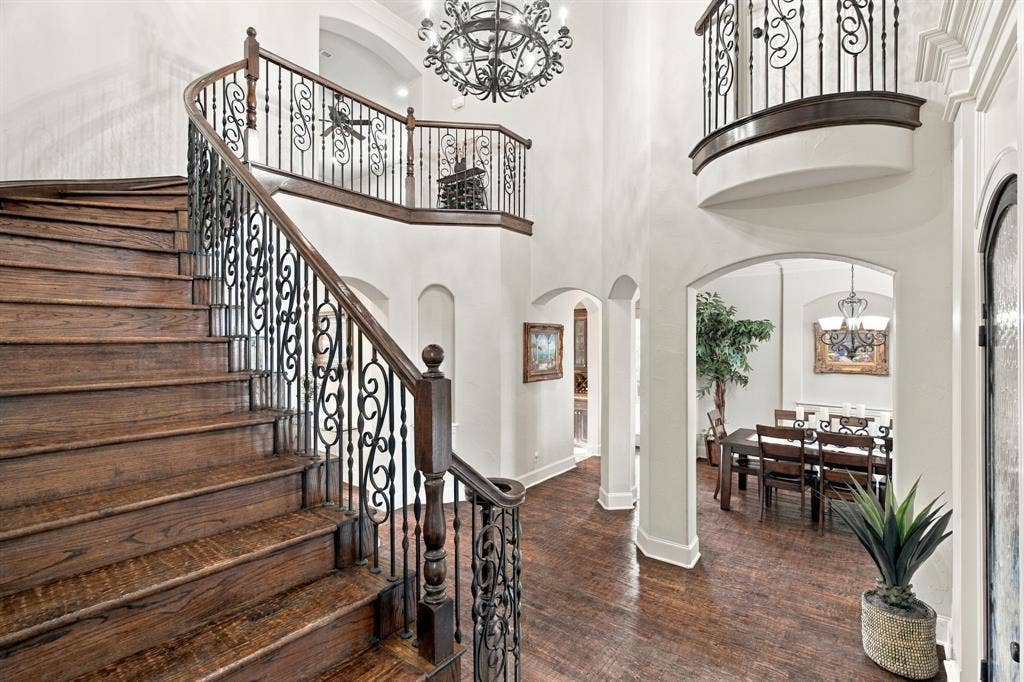 Grand foyer featuring a curved staircase with wood treads and ornate metal balusters, polished wood-finish flooring, soaring ceilings, a decorative chandelier, and arched architectural entryways