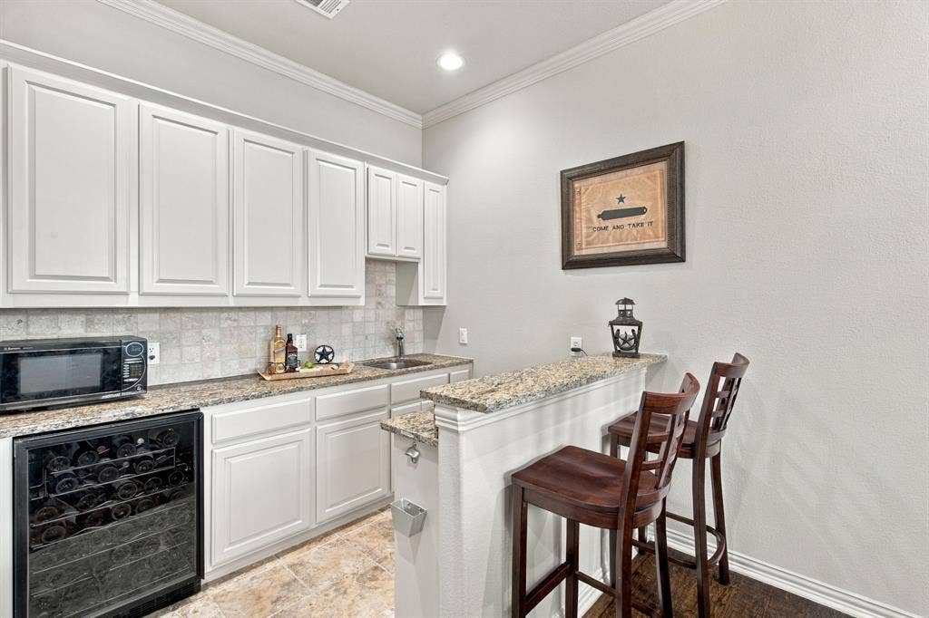 Wet bar featuring white cabinetry, stone-finish countertops, tile backsplash, built-in wine refrigerator, and sink