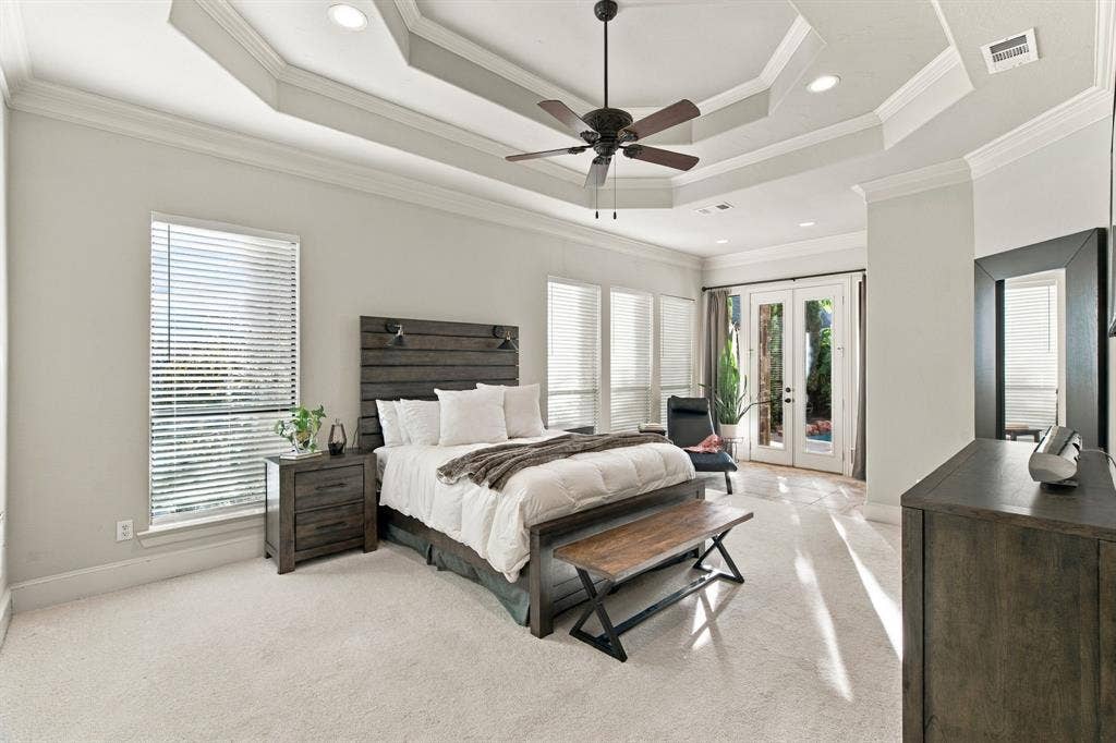 Tray ceiling with recessed lighting, central ceiling fan, neutral carpeting, multiple windows with blinds, and glass-paned doors