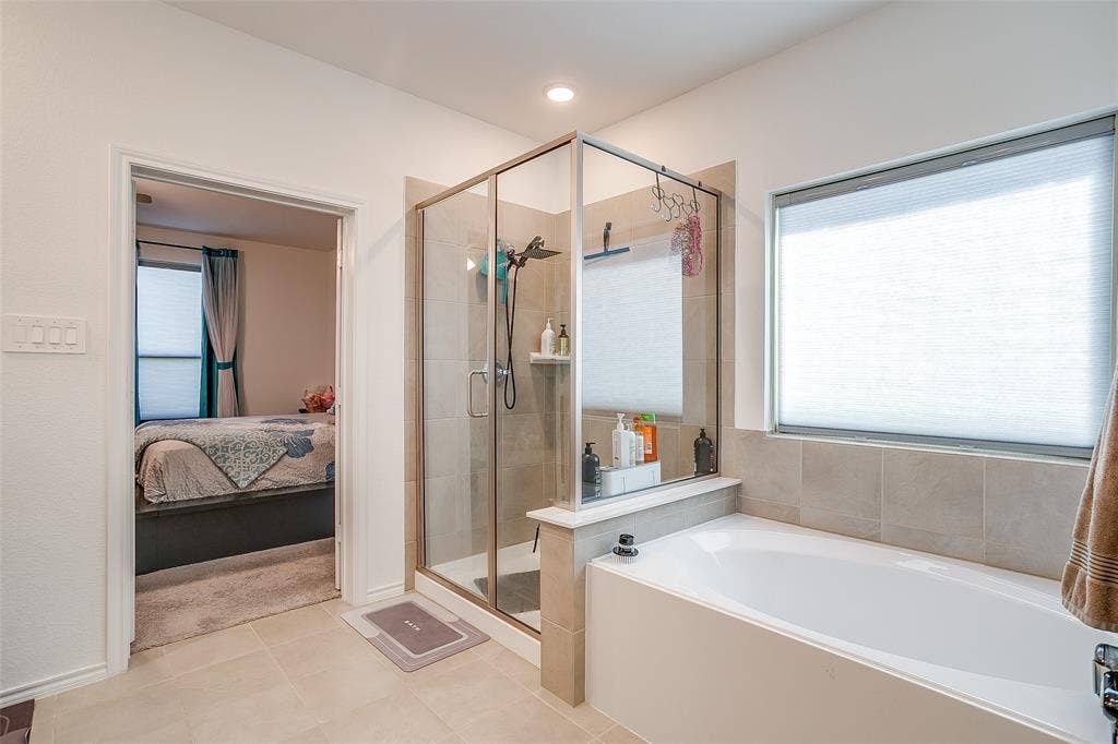 Full-size bathtub with a tiled surround, glass-enclosed shower, and neutral-toned wall and floor tile