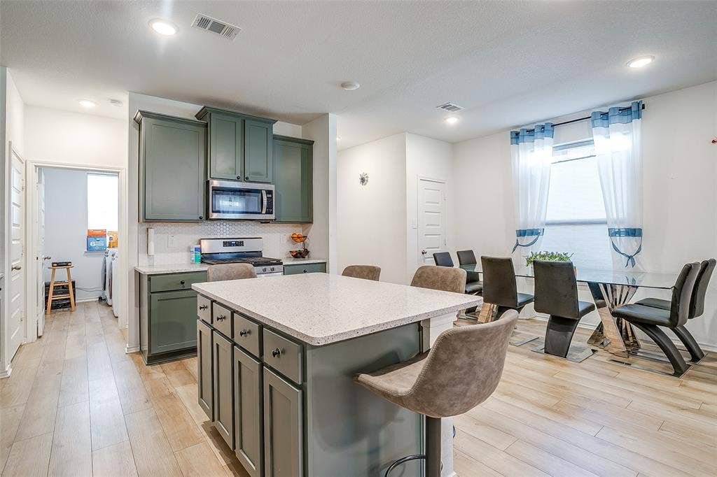 Kitchen with sage green cabinetry, stone countertops, stainless steel appliances, and wood-finish flooring