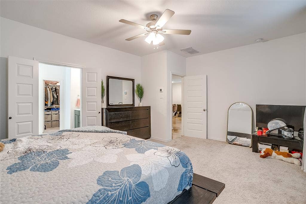 Bedroom featuring a ceiling fan, light-toned carpet flooring, white paneled doors, and an open entryway to a closet with built-in shelving