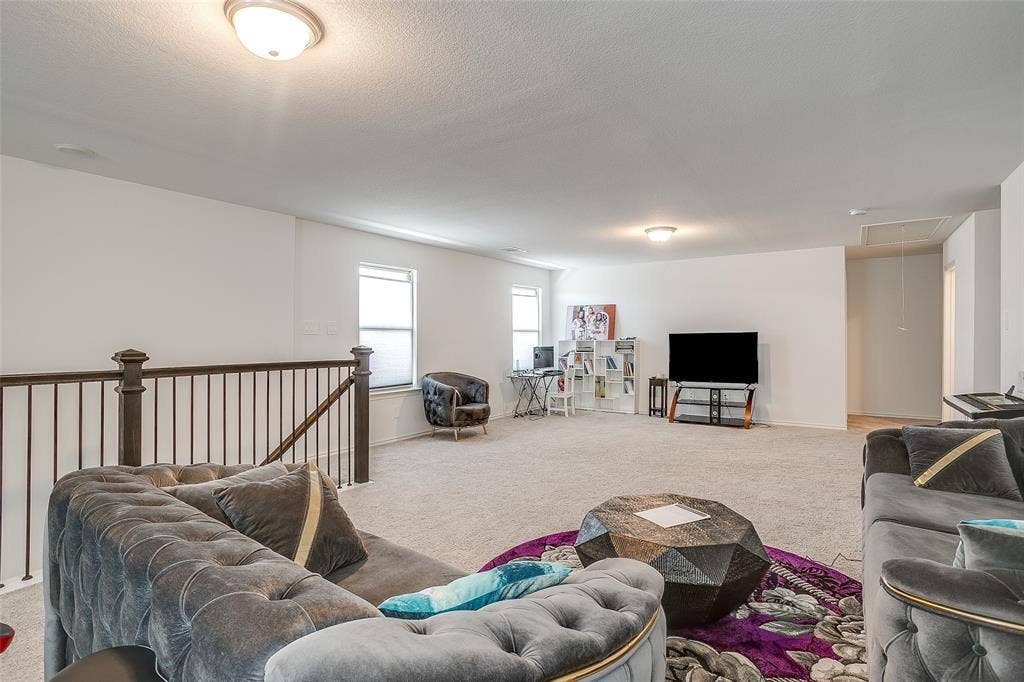 Expansive carpeted area with neutral walls, recessed lighting, and a dark wood and metal railing