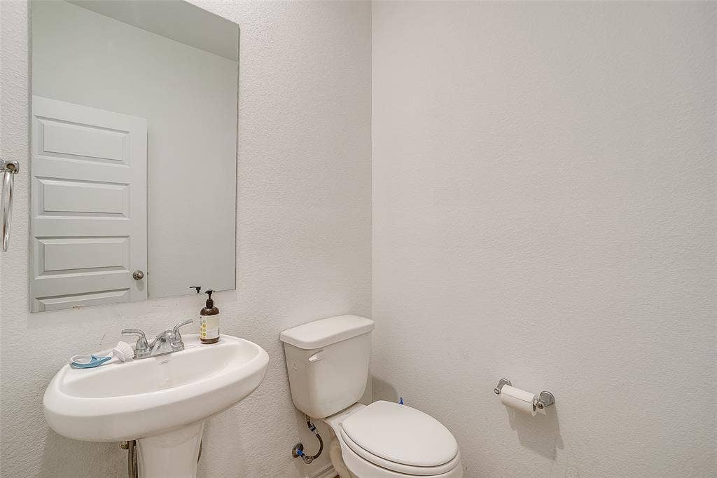 Pedestal sink with chrome faucet, wall-mounted mirror, and white paneled door