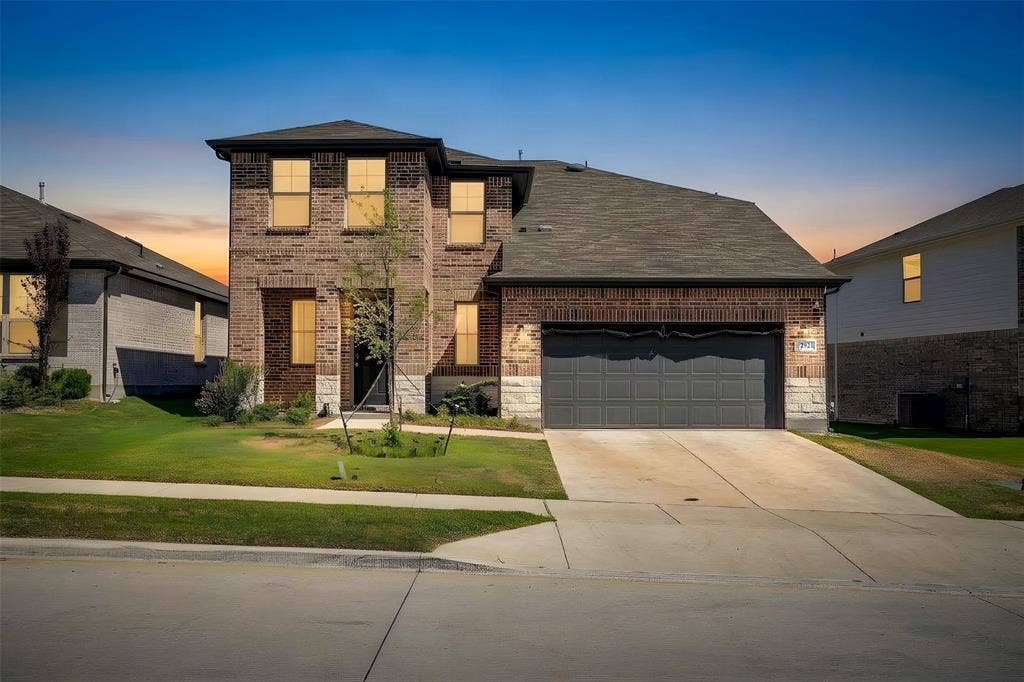 Brick and stone facade with a dark gray garage door, concrete driveway, and a manicured lawn