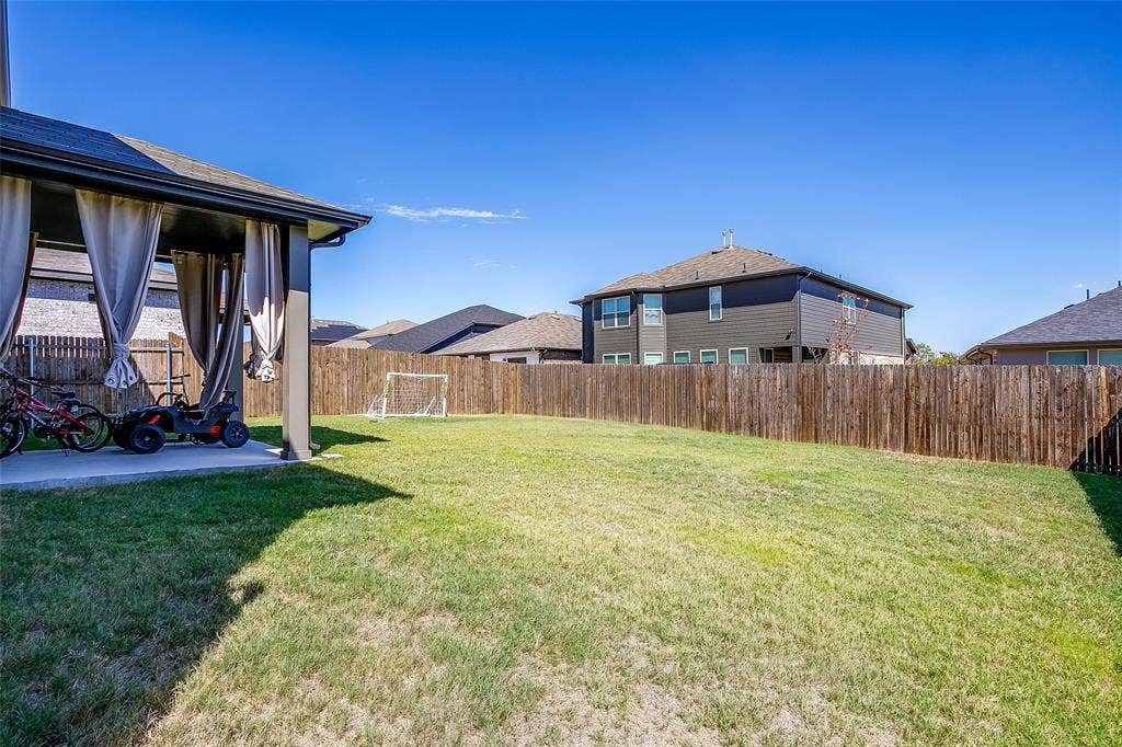 Expansive backyard with a lush lawn, privacy fencing, and a covered patio featuring drapes