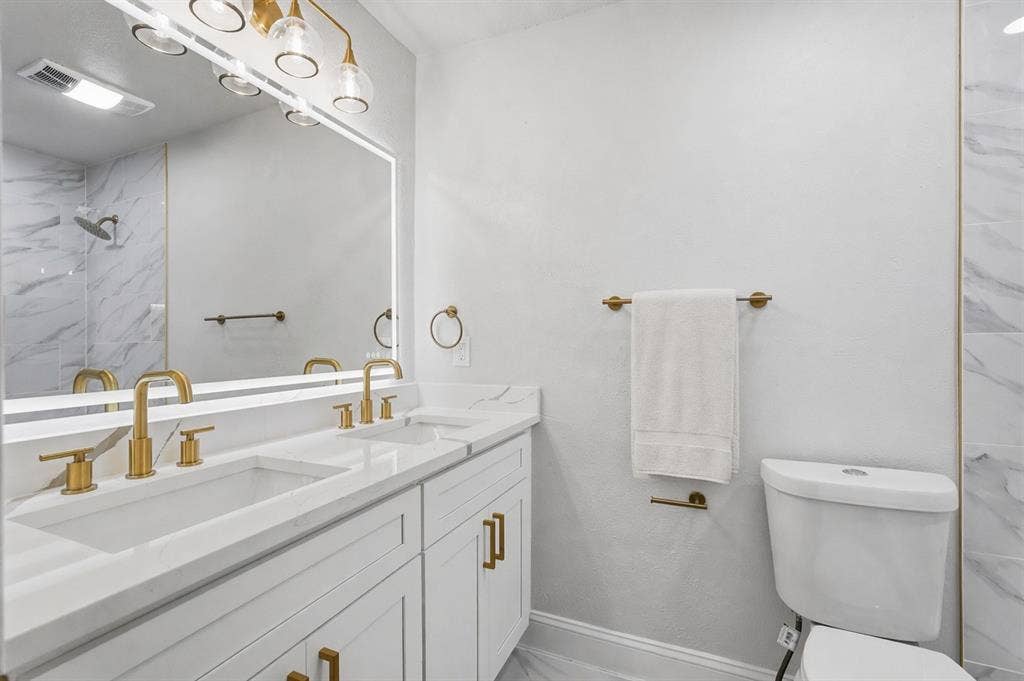 5514 Round Rock Road, Garland, TX 75044 Double vanity with white cabinetry, gold-finish hardware, and a single-slab countertop