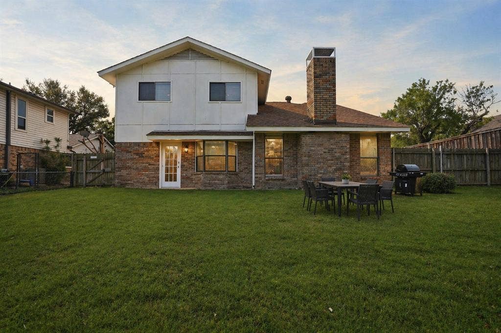 5514 Round Rock Road, Garland, TX 75044 Expansive yard featuring a brick and siding exterior, a prominent brick chimney, and a rear entry door with transom window