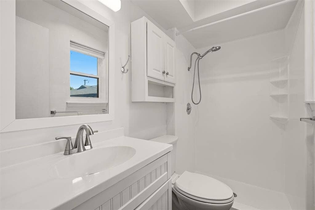 Spa-inspired bathroom featuring a floating vanity with quartz countertop and chrome faucet, white subway tile surround, frameless glass-enclosed shower with rainfall showerhead, toilet with elongated bowl, recessed medicine cabinet, and natural light from a picture window