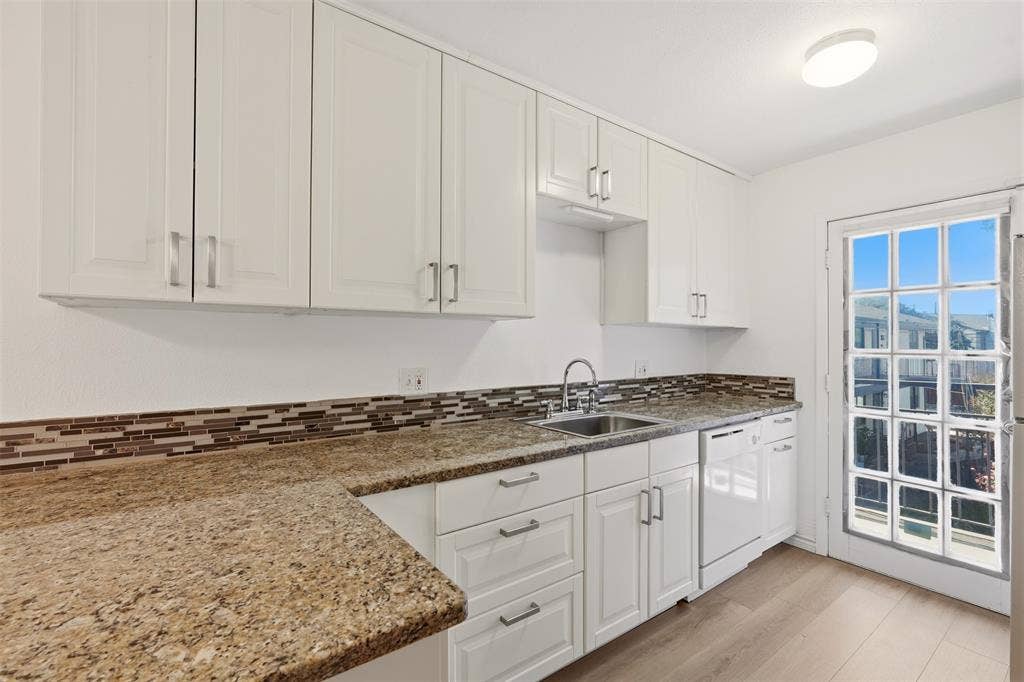 White cabinetry with brushed nickel hardware, granite-style countertops, mosaic tile backsplash, stainless steel sink, and wood-finish flooring