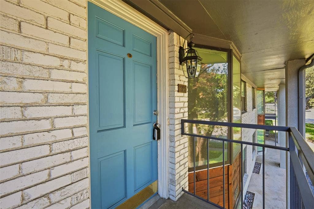White brick exterior with a panelled turquoise entry door, complemented by a black lantern-style sconce and a dark metal balcony railing