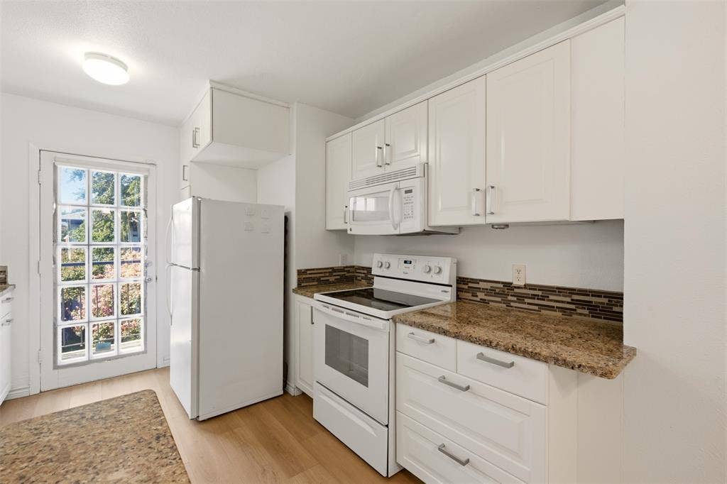 White cabinetry with modern hardware, stone countertops, integrated microwave, and wood-finish flooring